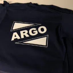 Granatowa koszulka z białym nadrukiem 'ARGO' otoczonym dwoma trójkątami, leżąca na płaskiej powierzchni.