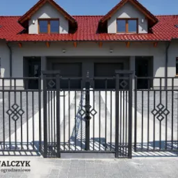 Nowoczesna, metalowa brama wjazdowa z dekoracyjnymi elementami rombowymi, zamontowana przed domem w Obrowcu. Widoczny panel z domofonem na słupku bramy.