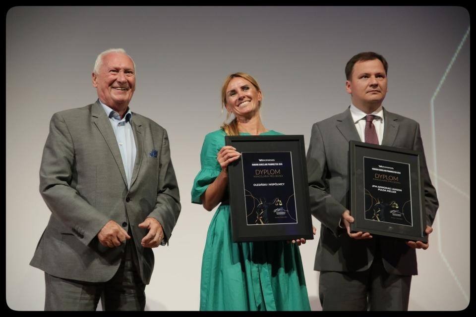 Trzy osoby na scenie trzymające oprawione dyplomy z nagrodami dla kancelarii prawnych, wręczone przez dziennik Rzeczpospolita.