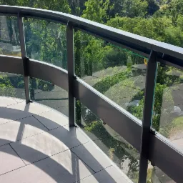 Szklana balustrada balkonu z widokiem na zieleń, na pierwszym planie butelka ze środkiem czyszczącym.