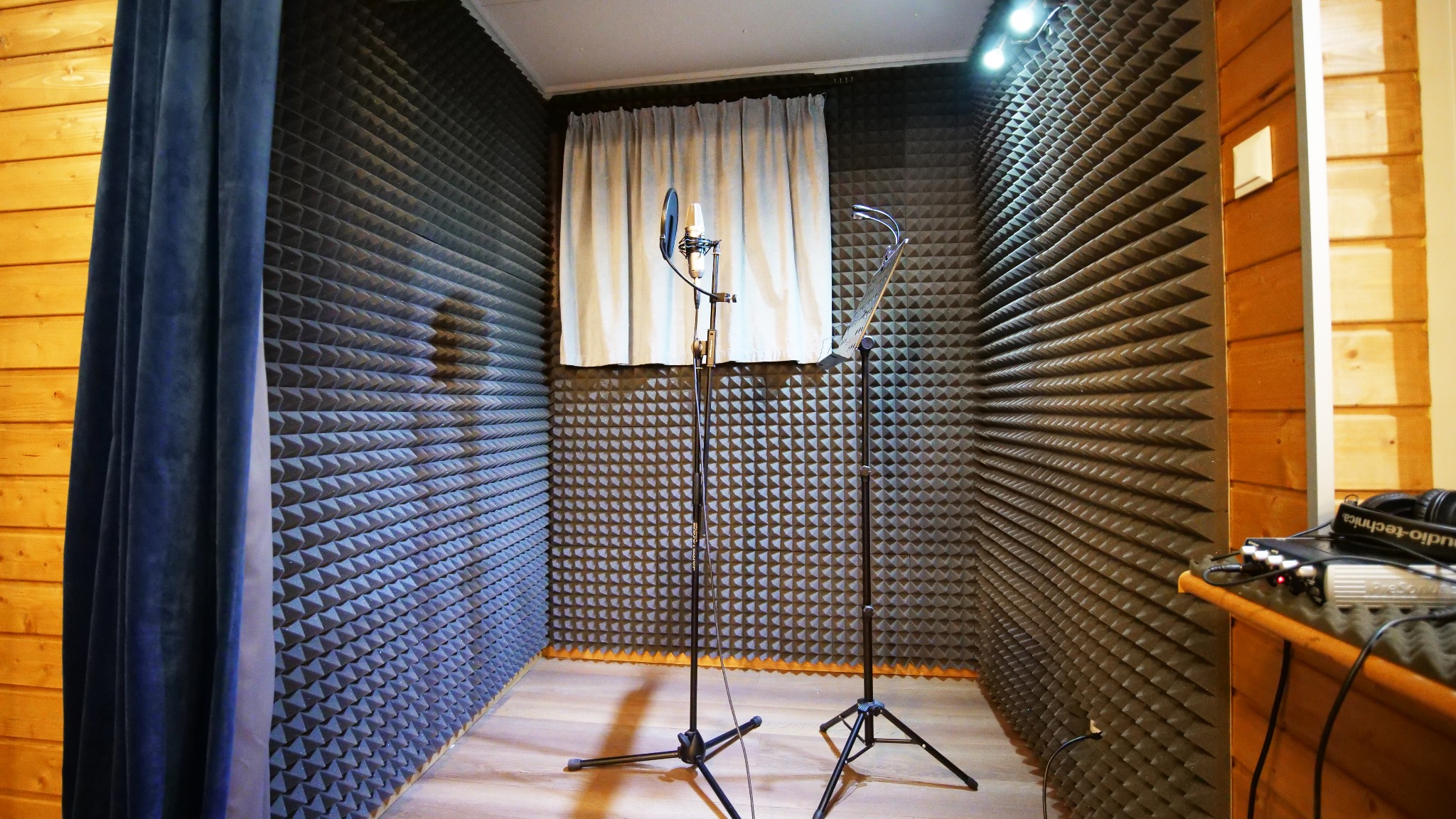 Wnętrze wyciszonego studia nagrań z mikrofonem na statywie i pulpit muzyczny, ściany pokryte panelami akustycznymi, drewniane wykończenie.