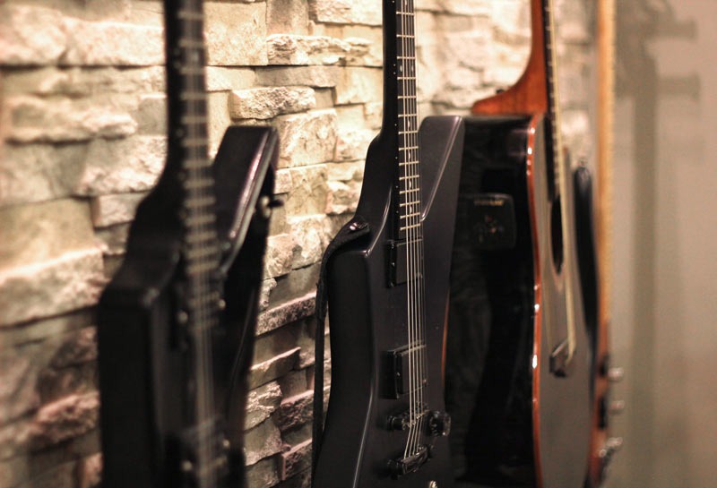 Trzy gitary (dwie elektryczne, jedna akustyczna) oparte o kamienną ścianę w pomieszczeniu z przytłumionym oświetleniem.