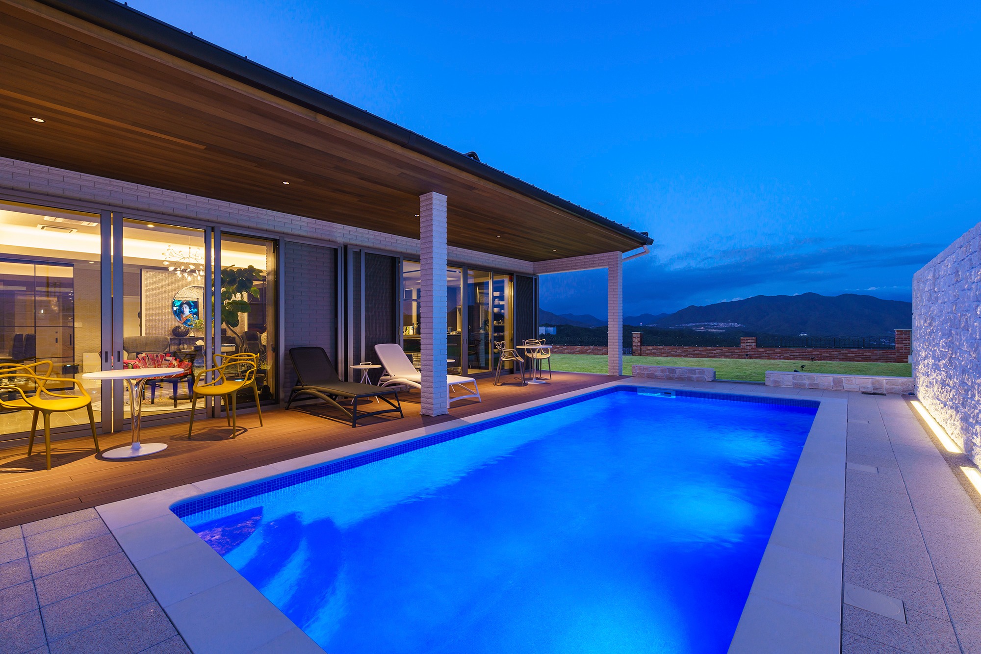 Oświetlony basen w Krakowie o zmierzchu, z widokiem na góry w tle, otoczony tarasem z meblami ogrodowymi i nowoczesną architekturą domu.