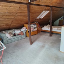 BŁYSK na PLUS - Zagracone poddasze ze skośnym drewnianym sufitem, meblami i stertą rzeczy. Widoczny fragment suszarki na pranie. Potencjalne zlecenie na opróżnianie mieszkania.