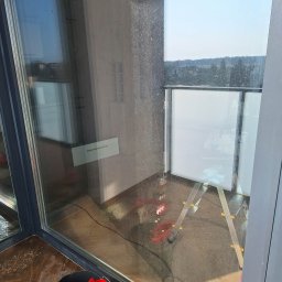 BŁYSK na PLUS - Brudna szyba okna balkonowego z widocznymi smugami i kurzem, obok drabina i wiadro z akcesoriami do mycia okien. Widok na zewnątrz przez czystą część szyby.