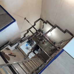 Alfa Welder - Widok z góry na montaż metalowej konstrukcji schodów w surowym wnętrzu, widoczne narzędzia, drabina aluminiowa i zabezpieczone taśmą malarską krawędzie podłogi.