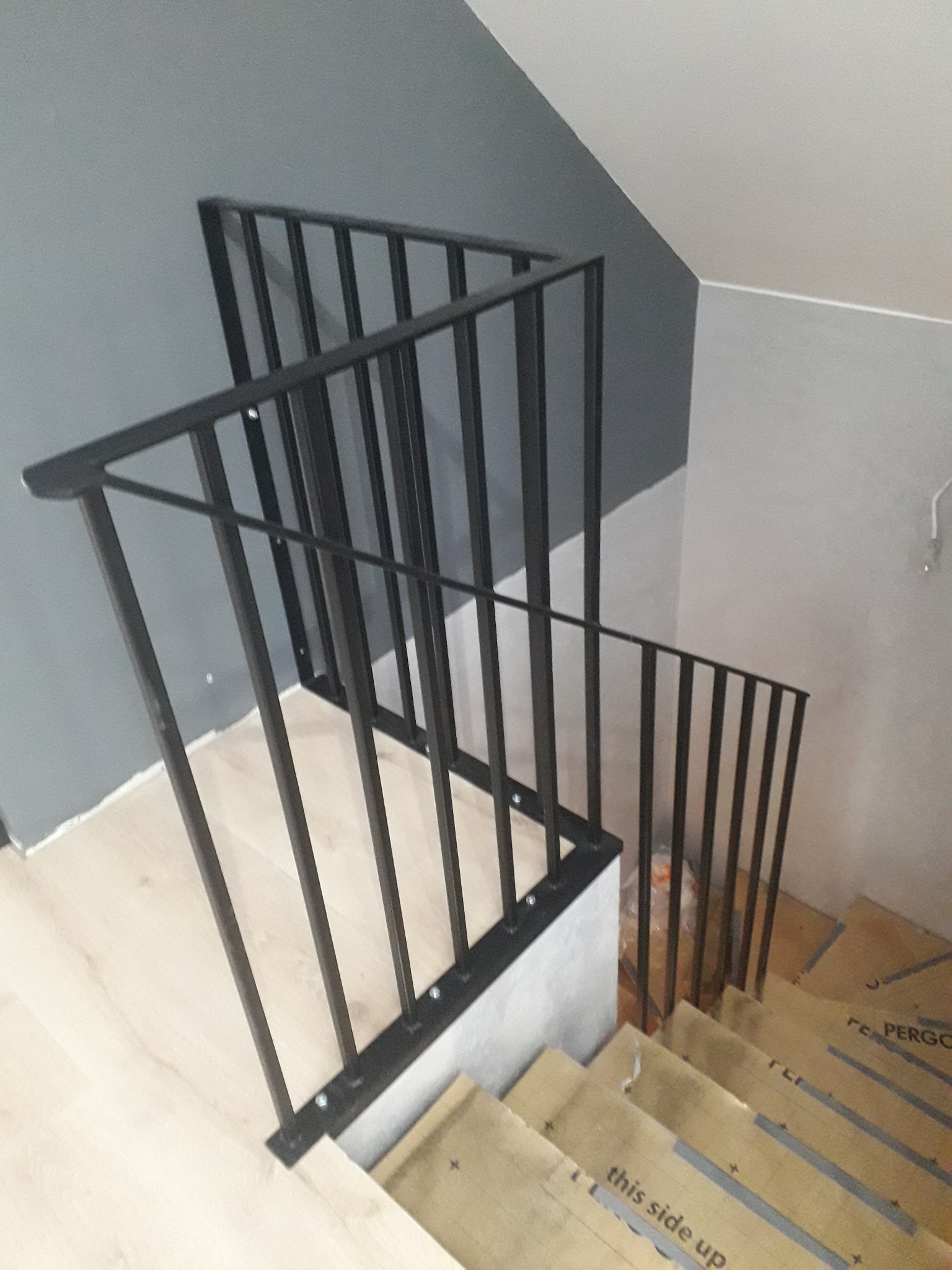 Nowoczesne schody z czarną metalową balustradą, widok z góry na zabezpieczone stopnie podczas montażu.