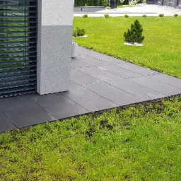 Nowoczesny taras z dużych, grafitowych płyt na trawniku, widok z góry, minimalistyczny design.