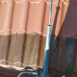 Czyszczenie dachu z blachodachówki za pomocą lancy ciśnieniowej, widoczny efekt różnicy czystości i zabrudzenia, zbliżenie na dyszę i fragment dachu.