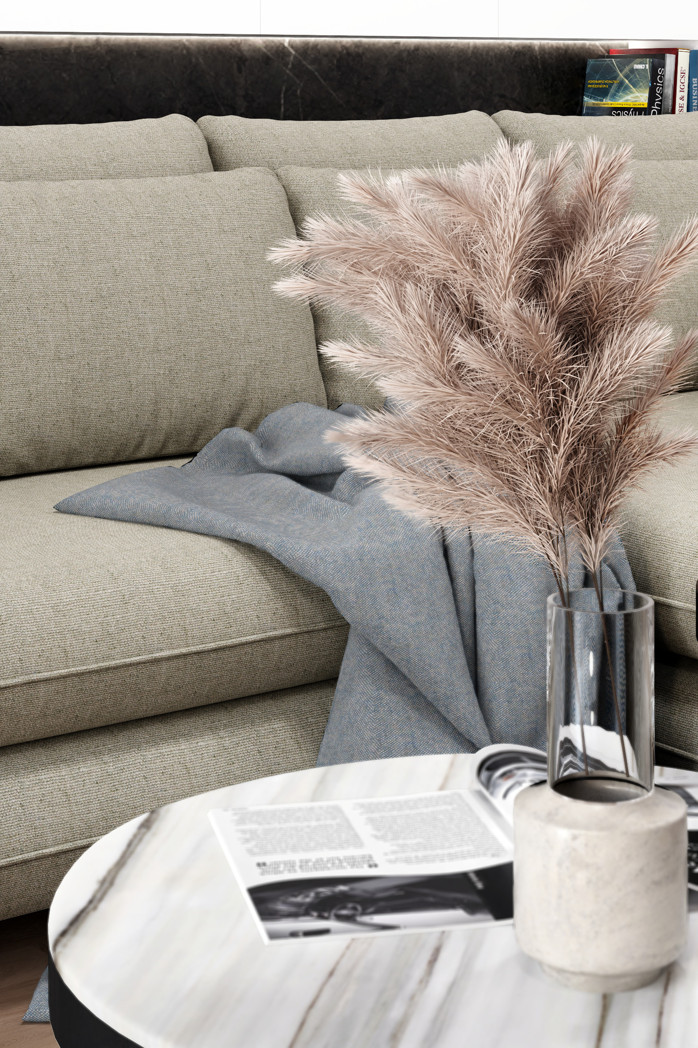 Beżowa sofa z poduszkami i błękitnym pledem. Na marmurowym stoliku wazon z puszystymi trawami i otwarta gazeta.