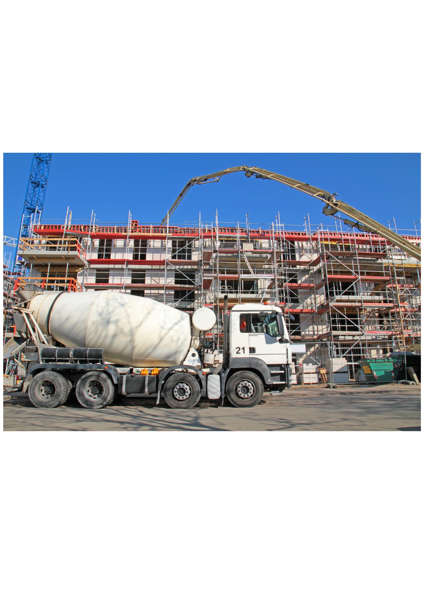 Biała betonomieszarka na budowie wielopiętrowego budynku z rusztowaniami, w tle niebieskie niebo i ramię pompy do betonu.