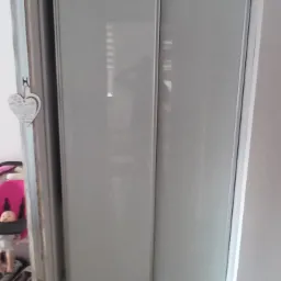 Wbudowana szafa z przesuwnymi, mlecznymi drzwiami, widoczna z perspektywy podłogi z paneli; po lewej stronie drzwi z dekoracyjnym sercem, w tle wózek dziecięcy.