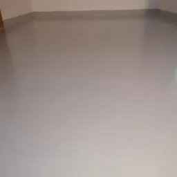 Gładka, jasnoszara posadzka w pomieszczeniu z listwami przypodłogowymi, oświetlona naturalnym światłem, ukazująca jednolitą powierzchnię.