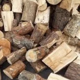 Stos pociętych kawałków drewna o różnej wielkości i kształcie, z widocznymi słojami i korą, ułożonych na ciemnej powierzchni.