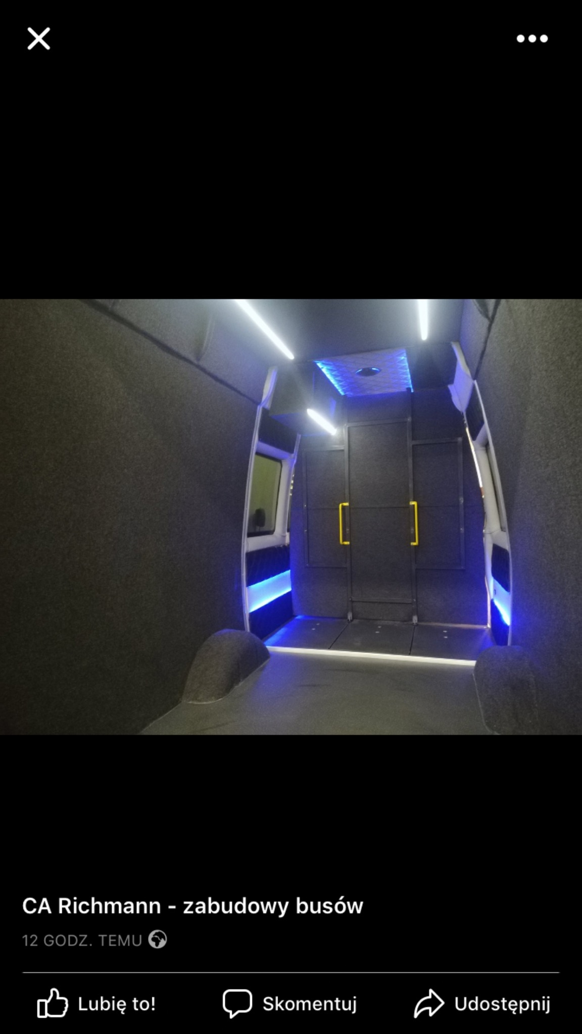 Wnętrze dostawczego busa po zabudowie, widok od tyłu, szare tapicerowane ściany, oświetlenie LED białe i niebieskie, czarne drzwi z żółtymi uchwytami.