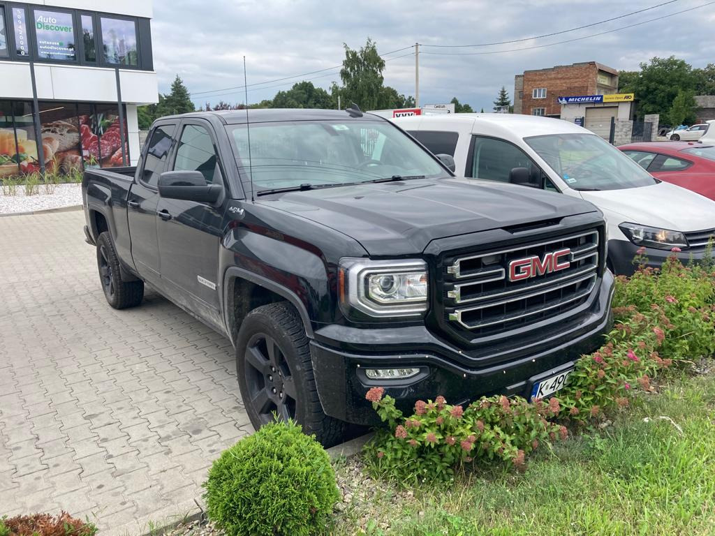 Czarny pickup GMC Sierra zaparkowany na kostce brukowej przed budynkiem z reklamą Auto Discover, widoczny numer rejestracyjny K-490.
