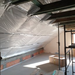 Prof-Man - Poddasze w trakcie ocieplania folią aluminiową, widoczne krokwie, ceglana ścianka kolankowa i rusztowanie.