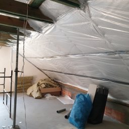 Prof-Man - Poddasze w trakcie ocieplania, widoczna folia paroizolacyjna na skośnych ścianach, rusztowanie, wełna mineralna w kartonie, oraz worki na odpady budowlane.