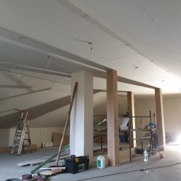 Prof-Man - Poddasze w Barlinku w trakcie remontu, widoczne płyty karton gips na suficie, konstrukcja szkieletowa z drewna, drabina i narzędzia, sylwetka osoby w tle przy oknie.