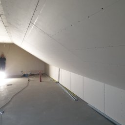 Prof-Man - Montaż płyt kartonowo-gipsowych na skośnym poddaszu, widoczne profile i narzędzia, osoba w tle. Świeżo położona wylewka podłogowa.