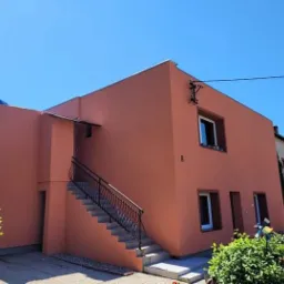 Dom jednorodzinny z nową elewacją w odcieniach terakoty, widoczne zewnętrzne schody z metalową balustradą i numer budynku '8'.