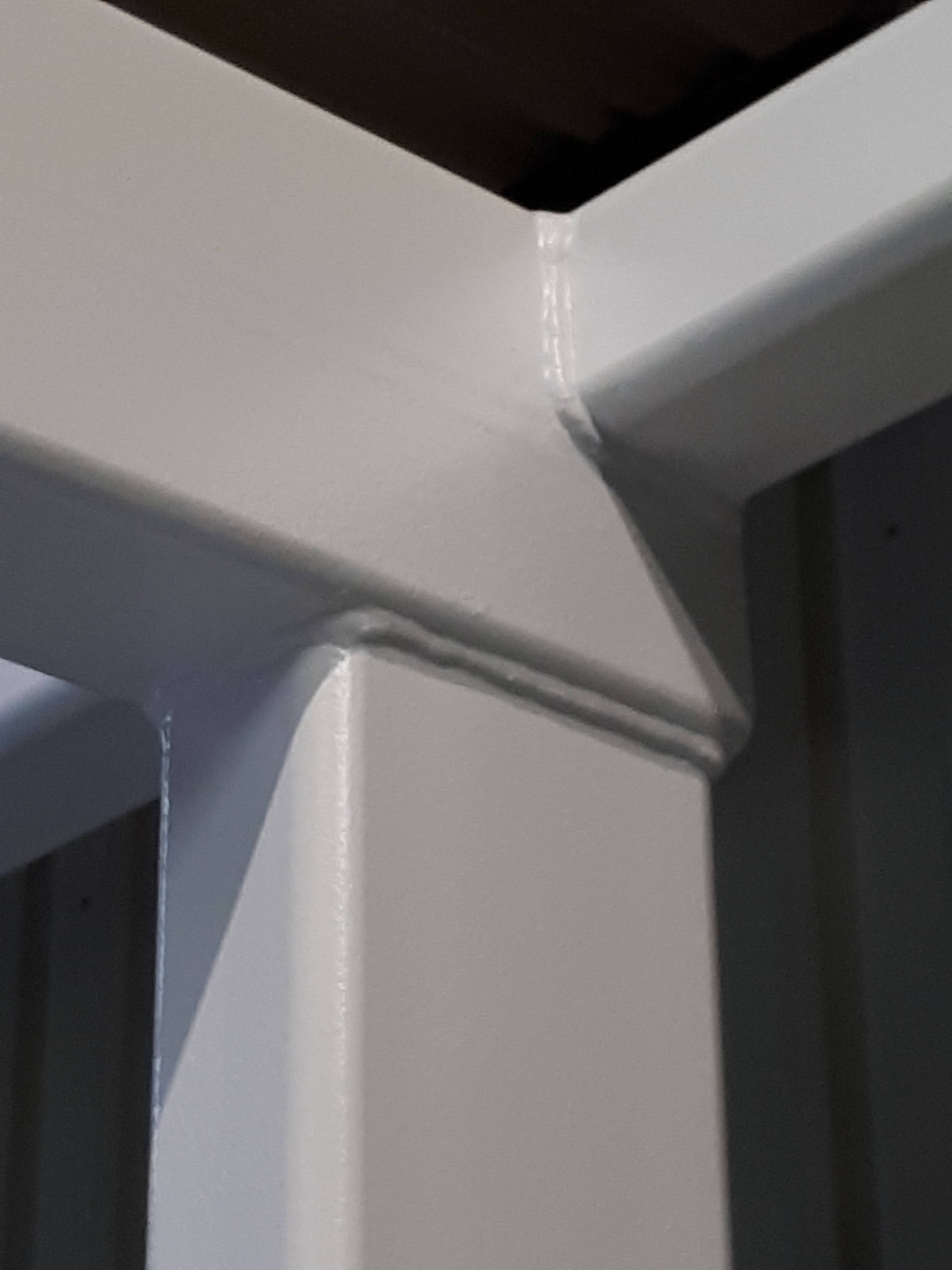 Detal złącza spawanej konstrukcji stalowej pomalowanej na biało, widoczny spaw i wykończenie powierzchni.