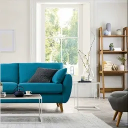 Jasne wnętrze salonu z turkusową sofą, drewnianym regałem i dużym oknem w białej ramie w tle.