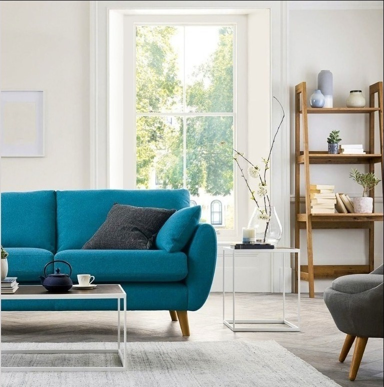 Jasne wnętrze salonu z turkusową sofą, drewnianym regałem i dużym oknem w białej ramie w tle.