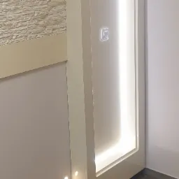 Fragment ściany z dekoracyjną, podświetlaną wnęką, wykończoną kamieniem dekoracyjnym, widoczny włącznik światła.