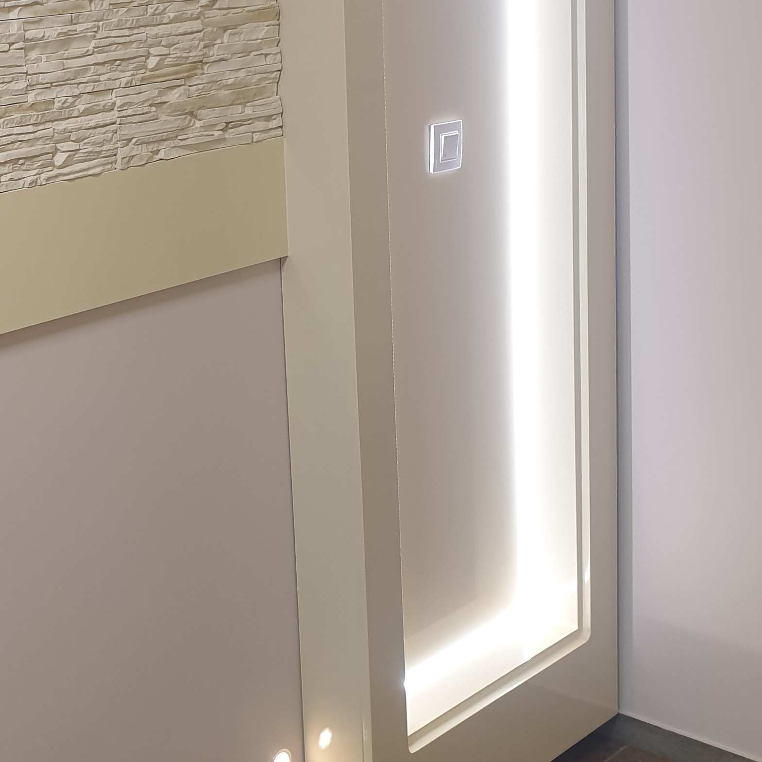 Fragment ściany z dekoracyjną, podświetlaną wnęką, wykończoną kamieniem dekoracyjnym, widoczny włącznik światła.