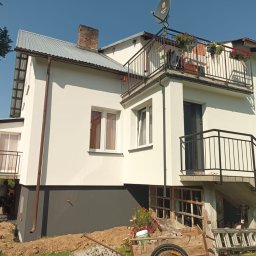 ŚWIECA INVEST ŁUKASZ ŚWIECZKOWSKI - Dwupiętrowy dom z balkonem w trakcie malowania elewacji, z widocznym fragmentem rusztowania i pracownikami w tle.