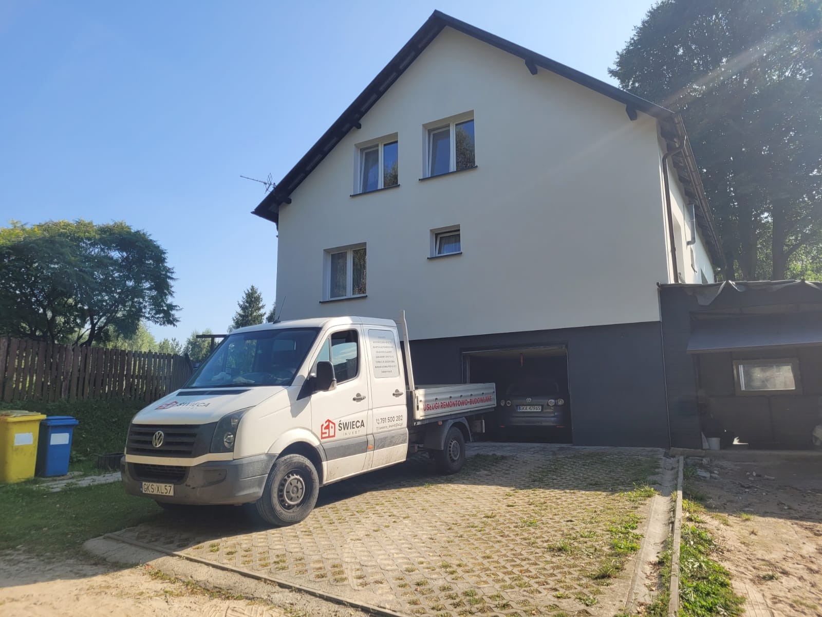 Świeżo otynkowany dom jednorodzinny z szarą podmurówką, na podjeździe stoi biały samochód dostawczy z logo firmy budowlanej Świeca Invest.