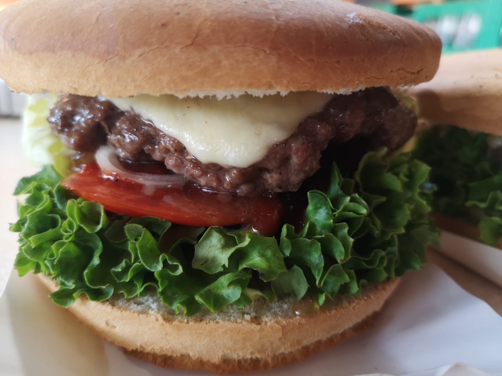 Apetyczny hamburger z wołowiną, serem cheddar, pomidorem, cebulą i świeżą sałatą lodową, widoczny drugi hamburger w tle.