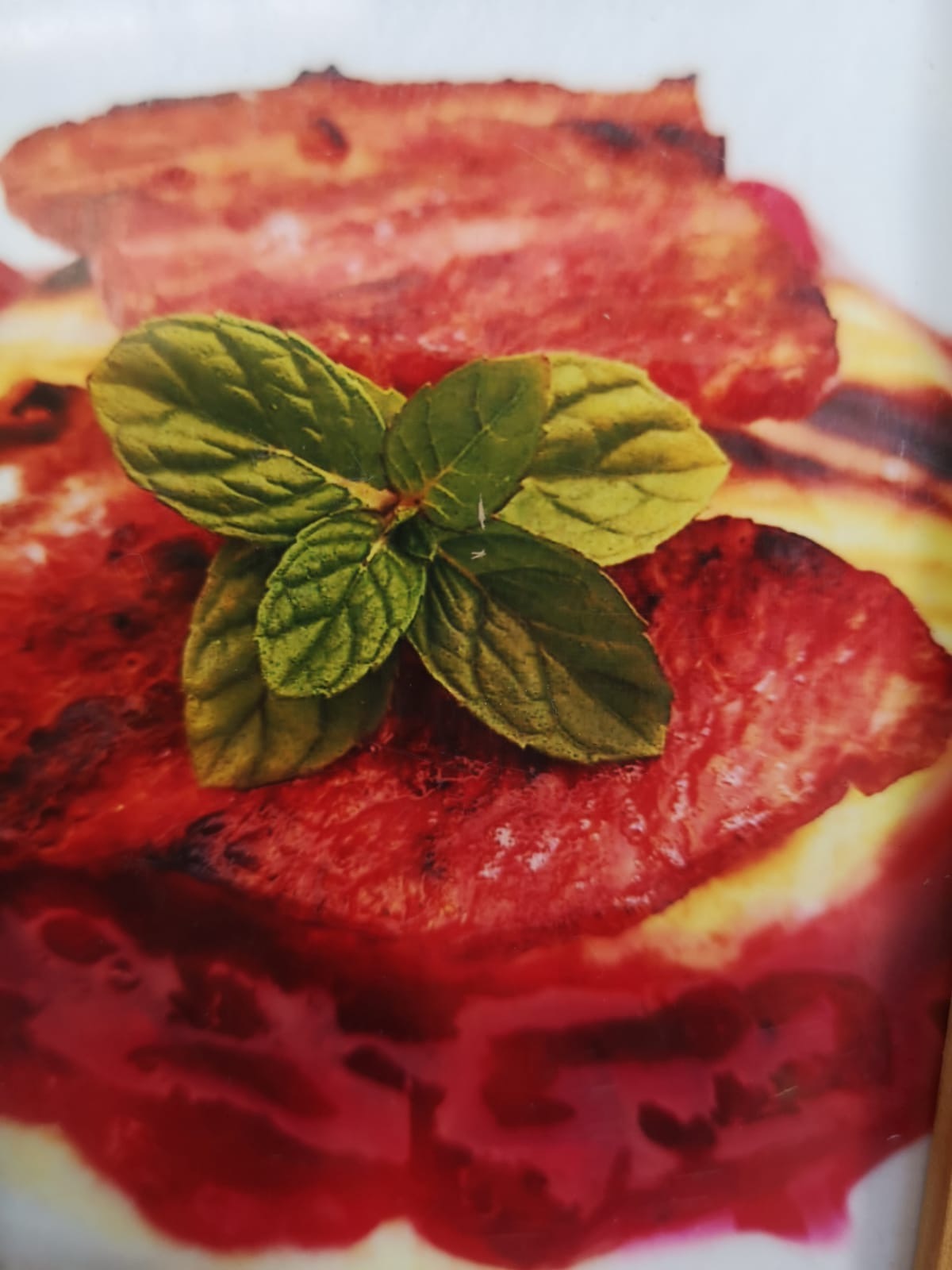 Grillowana wołowina z sosem i świeżą miętą, zbliżenie na talerz z widocznymi śladami grillowania.