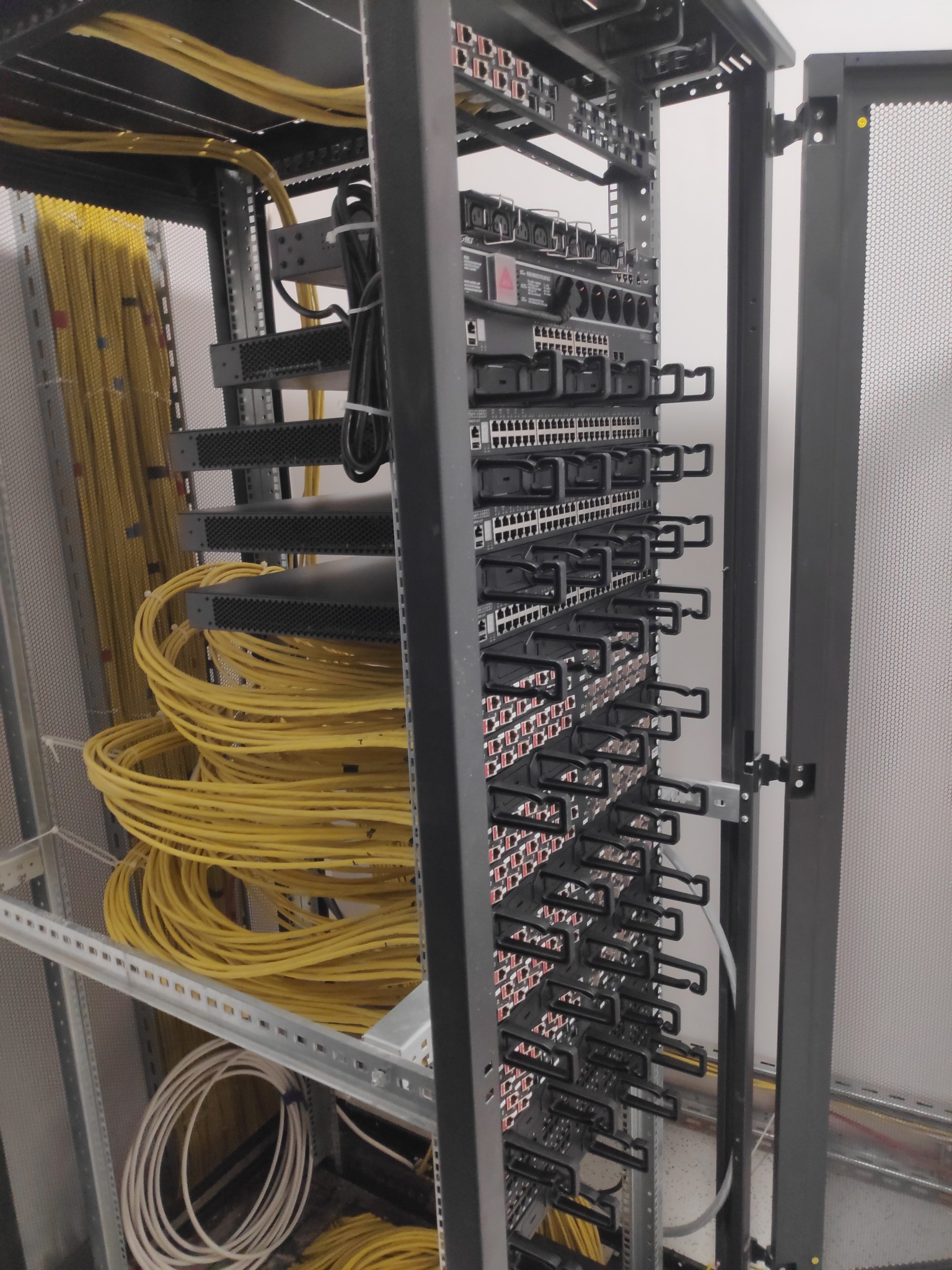 Szafa rack z uporządkowanymi, żółtymi kablami światłowodowymi i panelami krosowniczymi, widok z lekko otwartymi drzwiczkami szafy.