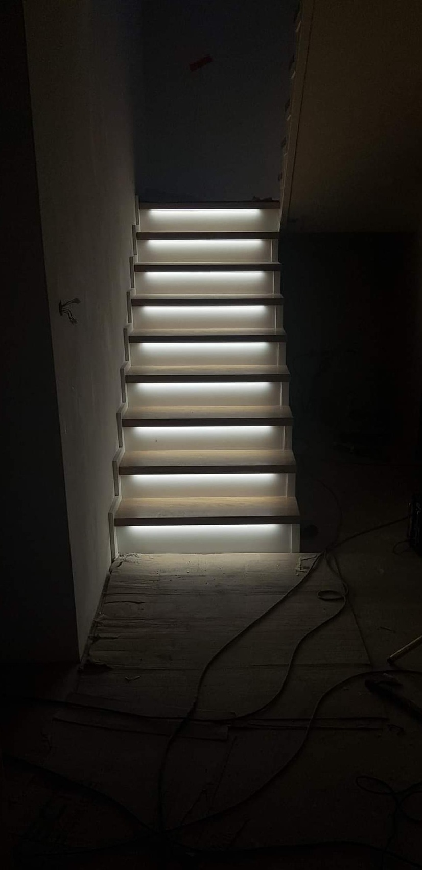 Schody drewniane z podświetleniem LED, widok od dołu, surowy stan wykończenia ścian i podłogi