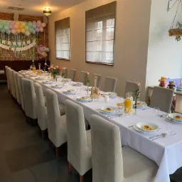 Uroczysty stół nakryty białym obrusem, przygotowany do przyjęcia gości we Wrocławiu, z dekoracjami balonowymi i kwiatowymi, aranżacja na przyjęcie okolicznościowe.