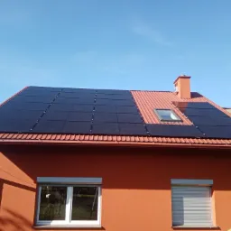 Czerwony dom z panelami słonecznymi na dachu z dachówki, widok z dołu na błękitne niebo.