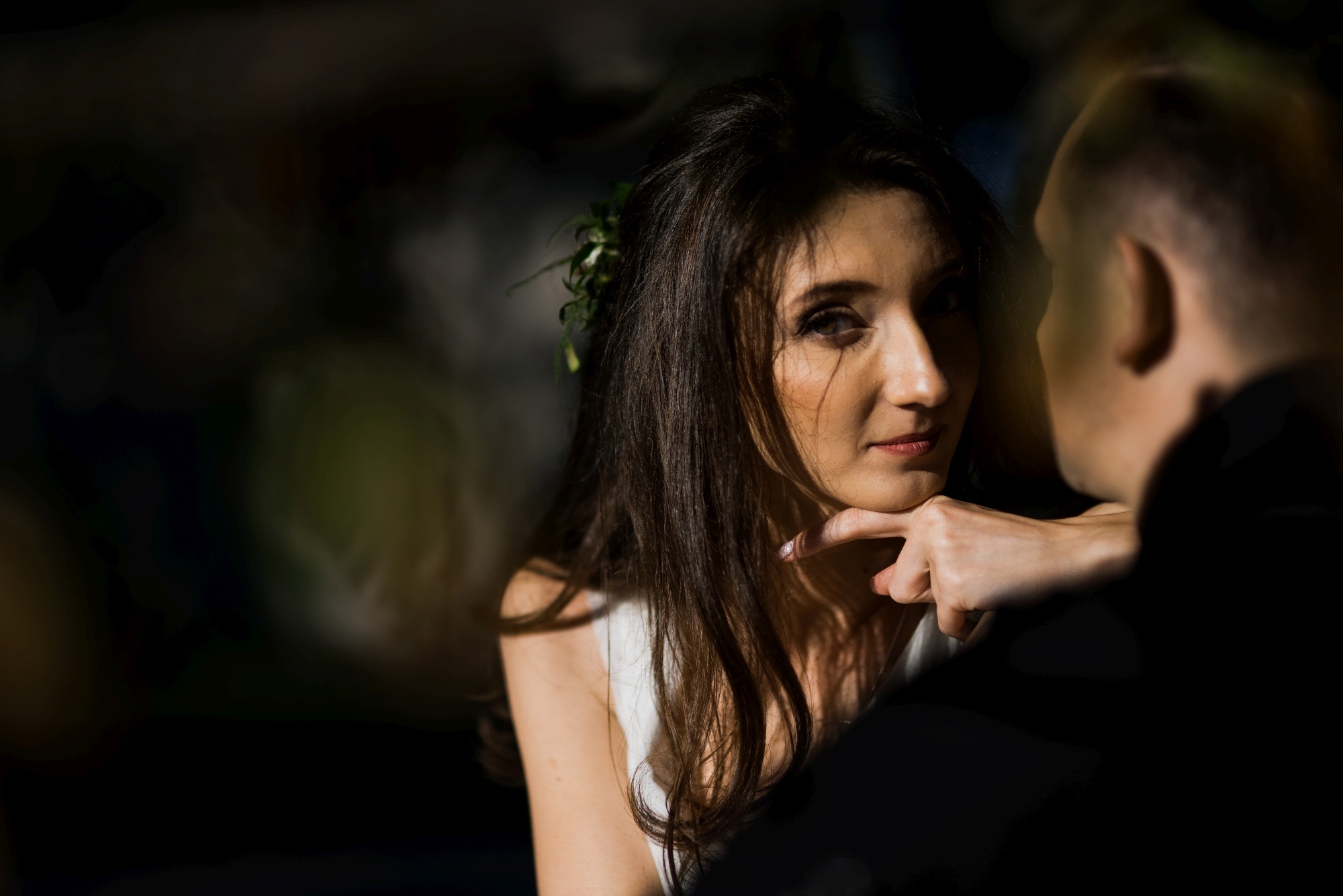 Portret kobiety z wiankiem we włosach, opierającej brodę na dłoni, spoglądającej na mężczyznę w ciemnym ubraniu, z delikatnym oświetleniem.