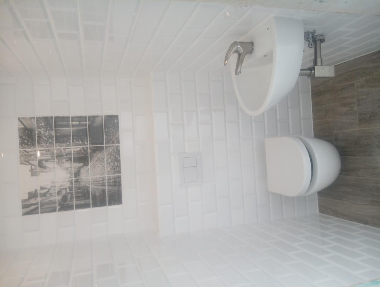 Nowoczesna łazienka z białą armaturą i płytkami typu metro, uzupełniona czarno-białą grafiką na ścianie.