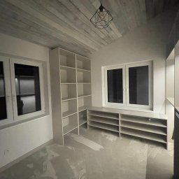 STOLARSTWO MEBLOWE JADWIGA SZAFLARSKA - Jasne, minimalistyczne wnętrze z regałami i szafkami pod oknem. Widoczny sufit z drewnianych desek i nowoczesna lampa. Podłoga zabezpieczona folią malarską.