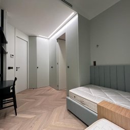 STOLARSTWO MEBLOWE JADWIGA SZAFLARSKA - Nowoczesny pokój z łóżkiem z tapicerowanym zagłówkiem, biurkiem i szafami w zabudowie. Parkiet w jodełkę, minimalistyczne oświetlenie LED.