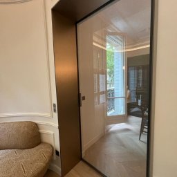 STOLARSTWO MEBLOWE JADWIGA SZAFLARSKA - Nowoczesna szafa wnękowa z przesuwnymi drzwiami ze szkła w eleganckim wnętrzu z parkietem w jodełkę i dekoracyjną sztukaterią.