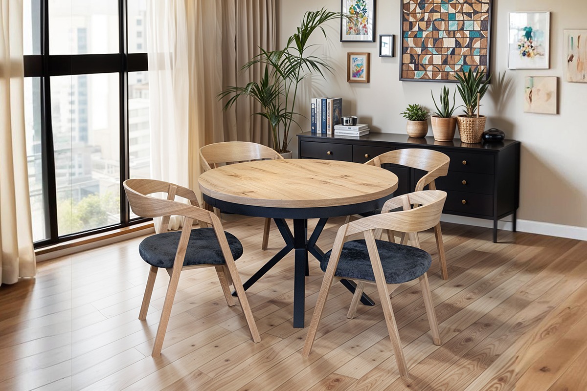 Okrągły stół z blatem drewnianym i czarną podstawą w nowoczesnej jadalni z krzesłami o jasnym drewnie i ciemnoszarym obiciu. W tle okno i komoda.