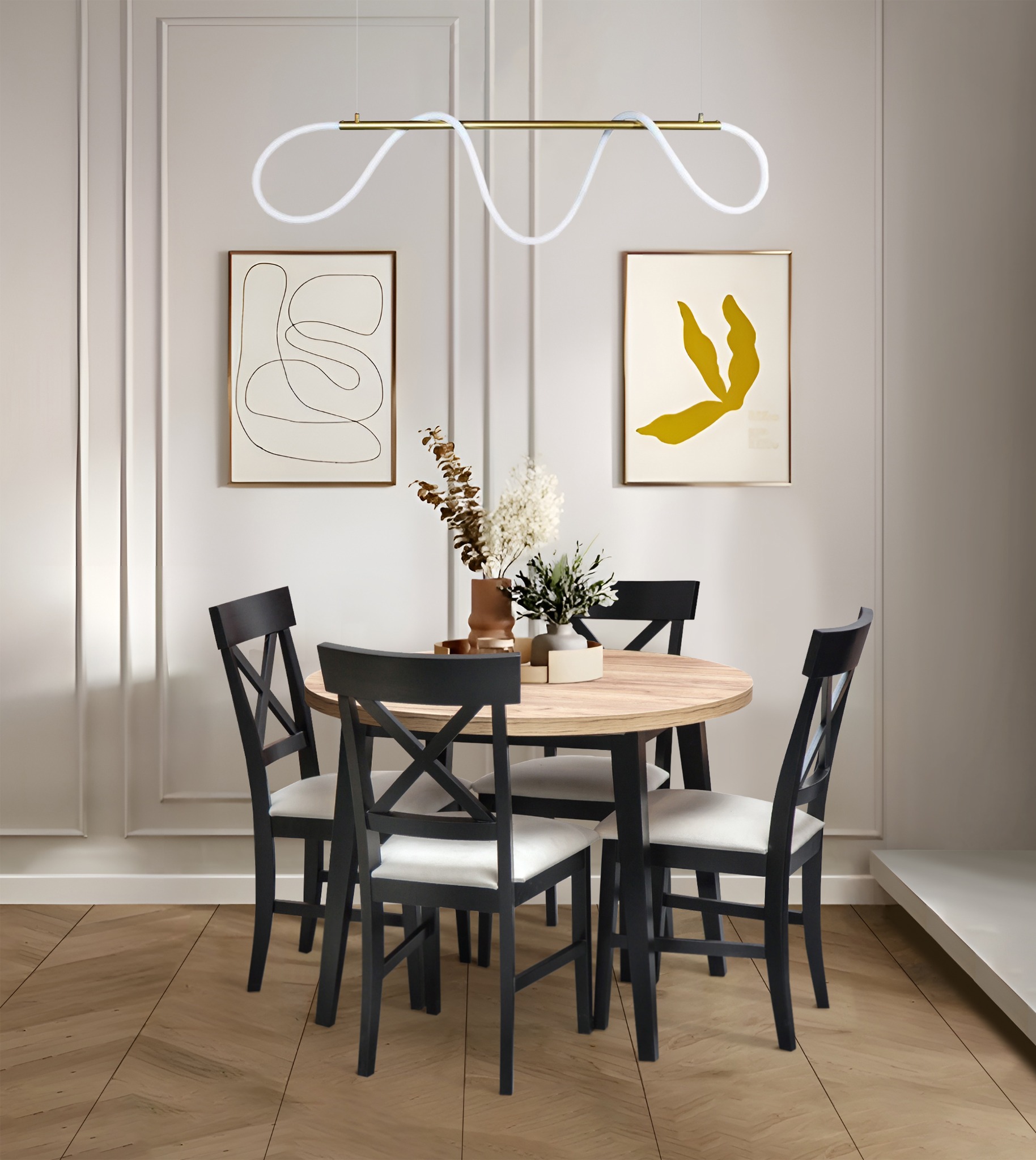 Okrągły stół z blatem drewnianym i czarnymi krzesłami w jasnym wnętrzu. Nad stołem designerska lampa. Na ścianie dekoracyjne obrazy w złotych ramach.