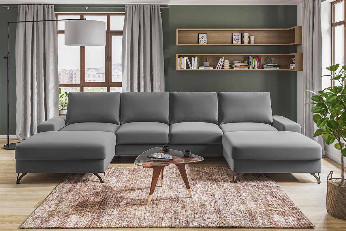 Szara, modułowa sofa narożna z podnóżkiem w nowoczesnym salonie. Na stoliku kawowym filiżanki i gazeta. W tle półki na ścianie i okno z zasłonami.