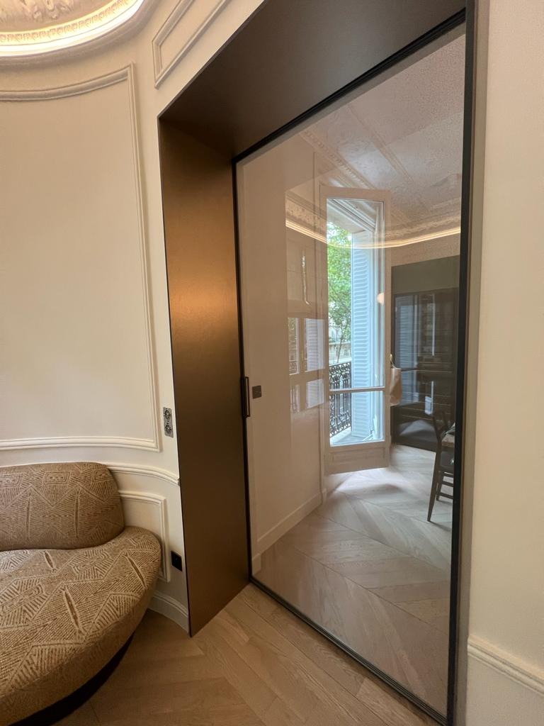 Nowoczesna szafa wnękowa z przesuwnymi drzwiami ze szkła w eleganckim wnętrzu z parkietem w jodełkę i dekoracyjną sztukaterią.