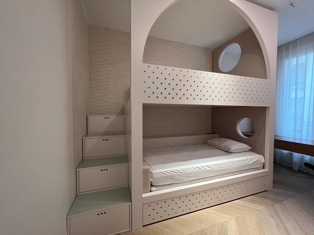 Różowe łóżko piętrowe z szufladami i schodkami w pokoju dziecięcym. Nietypowy design z okrągłymi okienkami. Realizacja z Łękawicy.