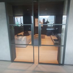 Nord-House - Nowoczesne, dwuskrzydłowe drzwi przesuwne z czarnymi szprosami, oddzielające salon z jasną podłogą i sofą od korytarza. Widok na góry za oknem w salonie.