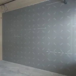 Wnętrze domu w trakcie wykańczania: drewniana ściana, zamontowana płyta karton gips z nadrukiem, widoczne instalacje pod sufitem, surowy beton na podłodze.